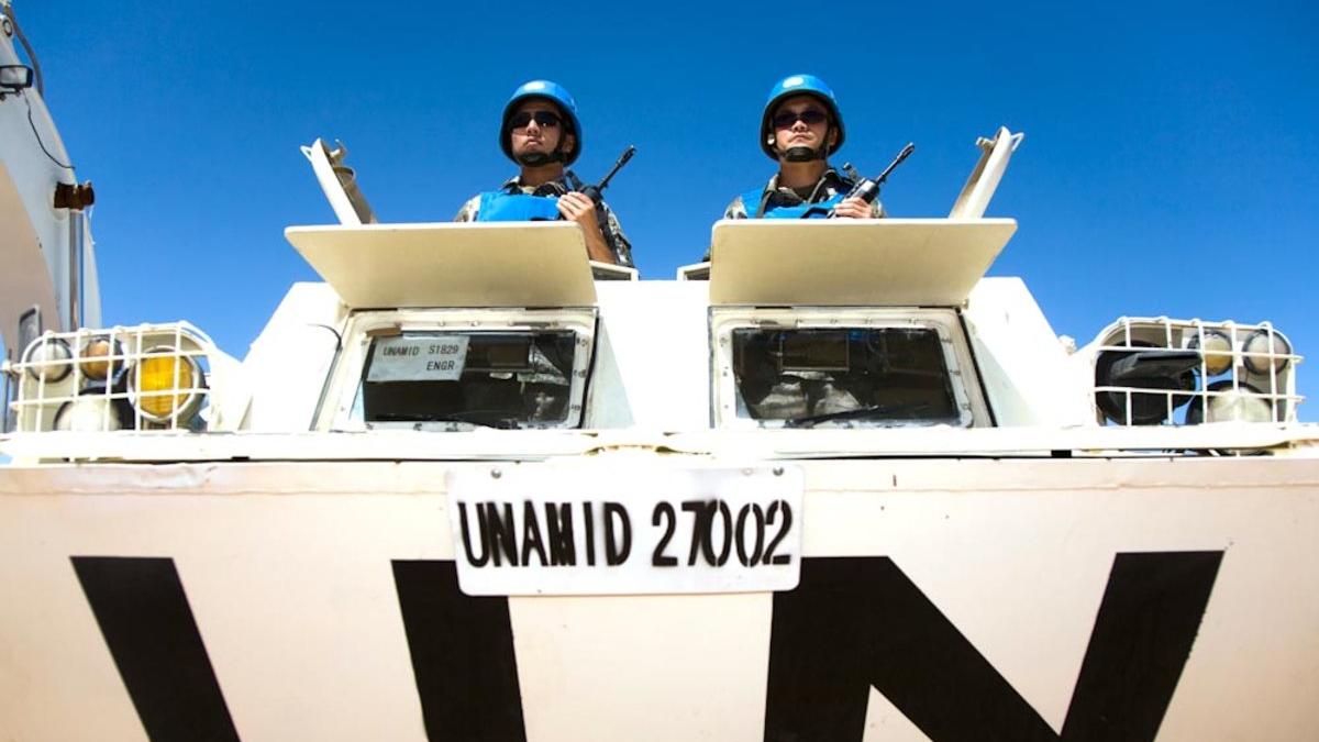 Two peacekeepers standing out of the hatch of a tank, each holding a weapon.