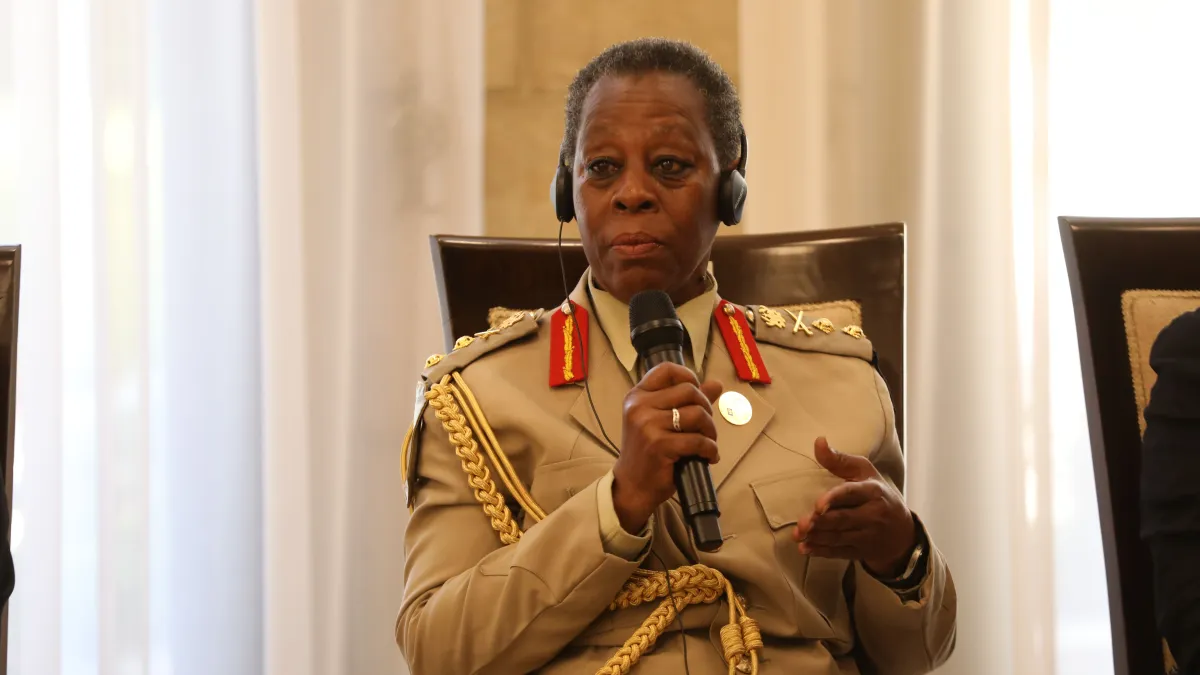 A uniformed official wearing a headset speaks into a handheld microphone while seated during a formal conference or diplomatic meeting.