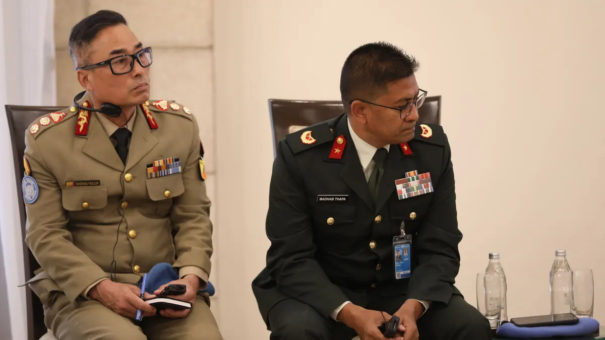 Two uniformed conference participants wearing headsets sit attentively with notepads and translation devices during a formal meeting.