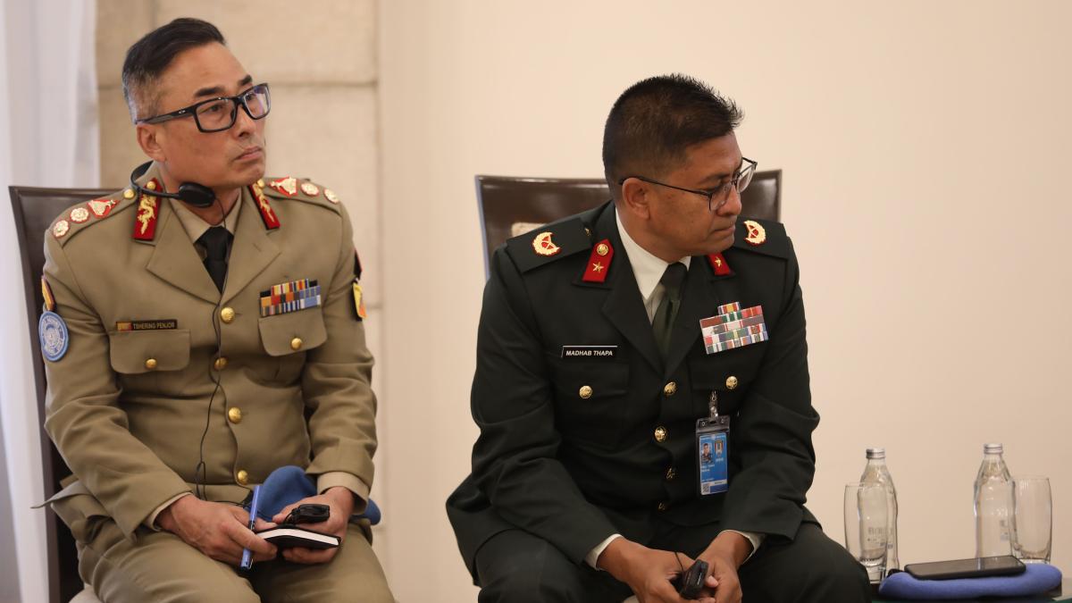 Two uniformed conference participants wearing headsets sit attentively with notepads and translation devices during a formal meeting.