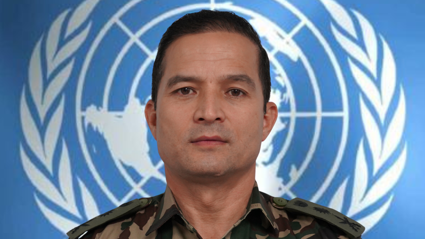 A headshot of a man in military uniform standing in front of the UN logo