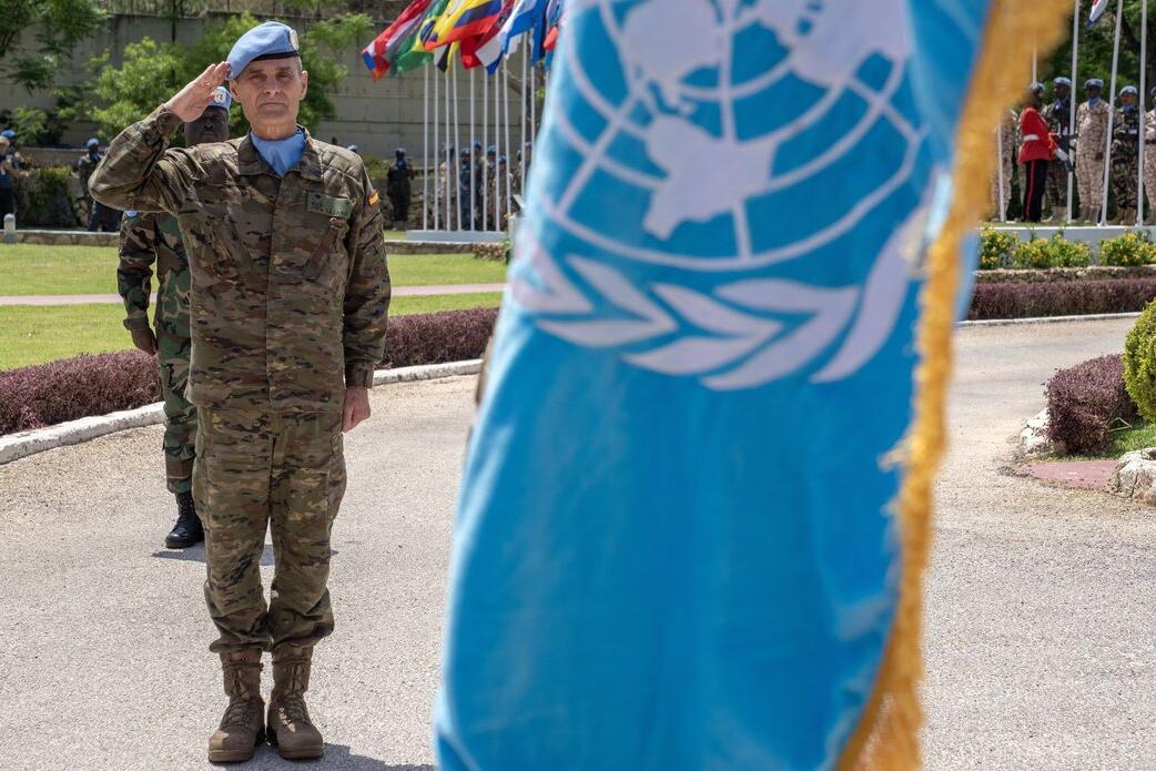 A peacekeeper salutes behind a UN flag.