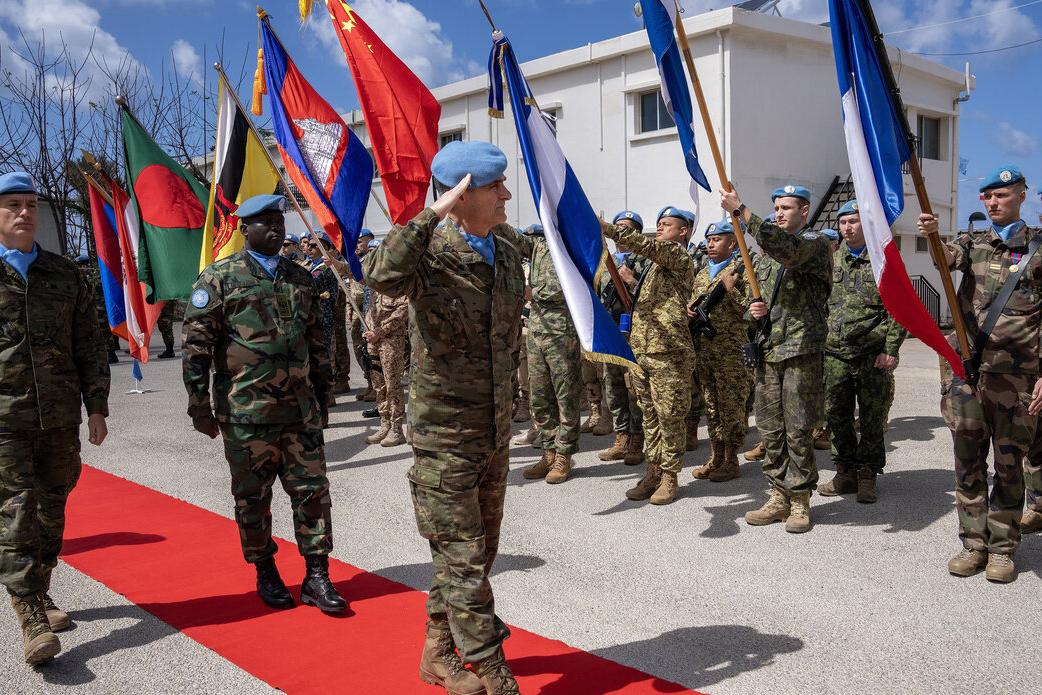 Peacekeepers hold flags as the Force Commander salutes.