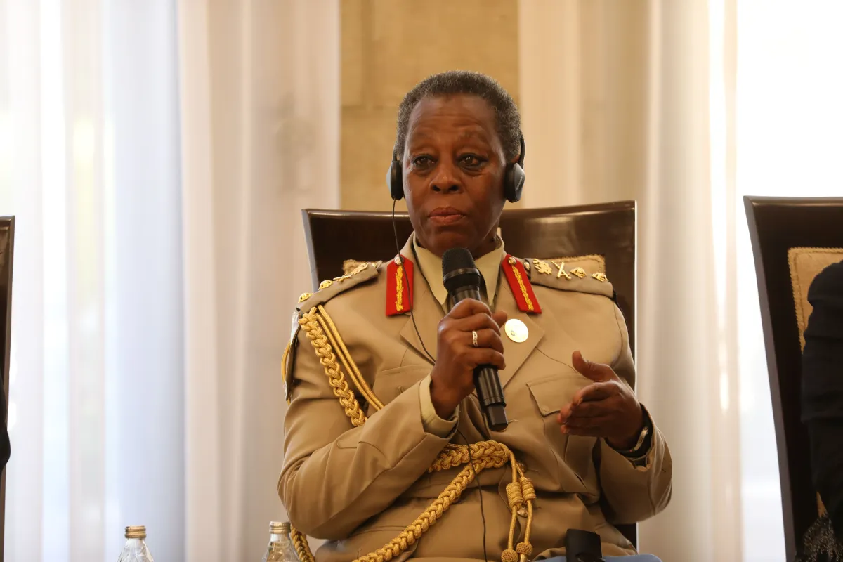 A uniformed official wearing a headset speaks into a handheld microphone while seated during a formal conference or diplomatic meeting.