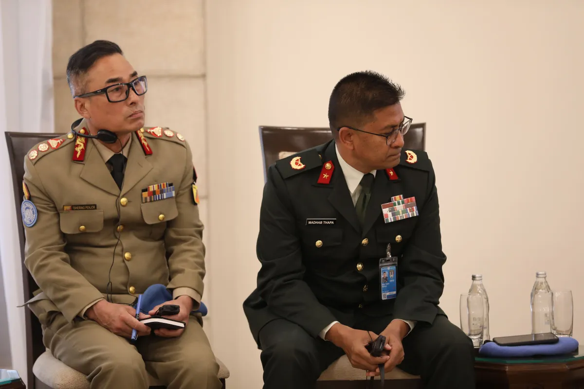 Two uniformed conference participants wearing headsets sit attentively with notepads and translation devices during a formal meeting.