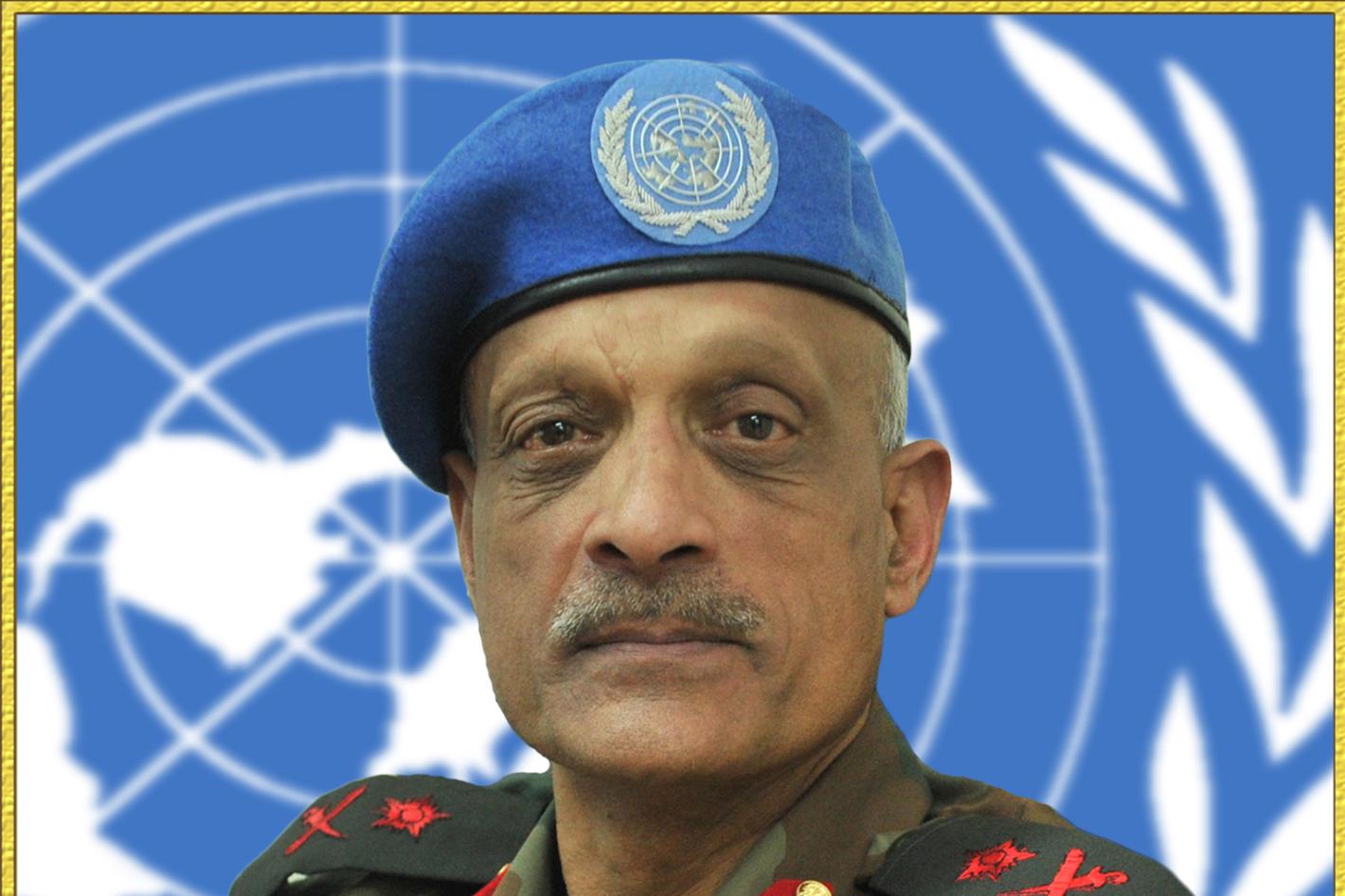 A man in military uniform with a blue beret sits in front of the UN logo