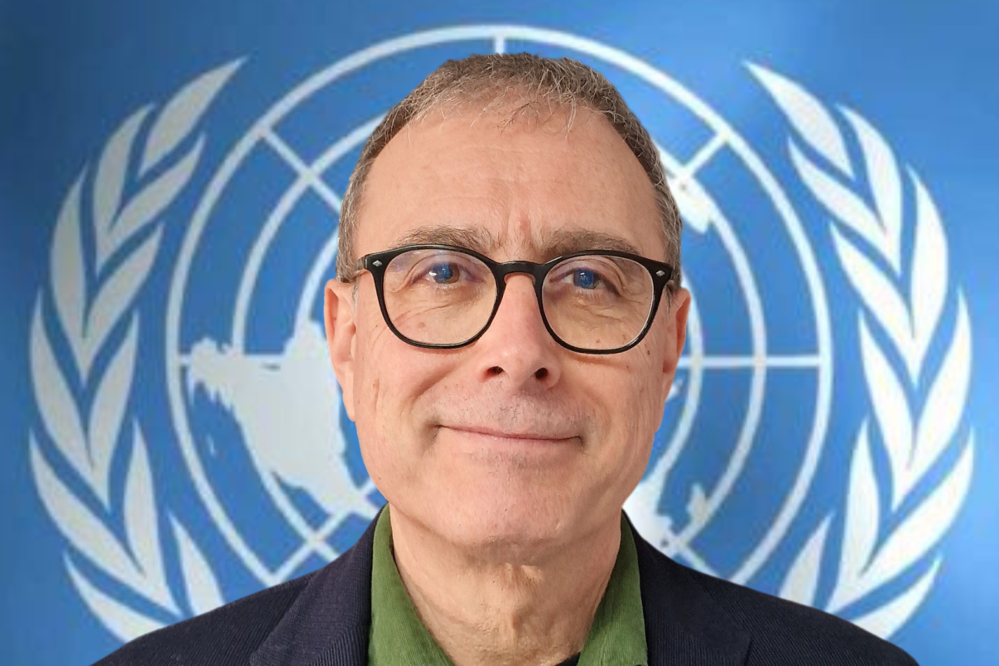 A headshot of a man in glasses in front of a UN logo