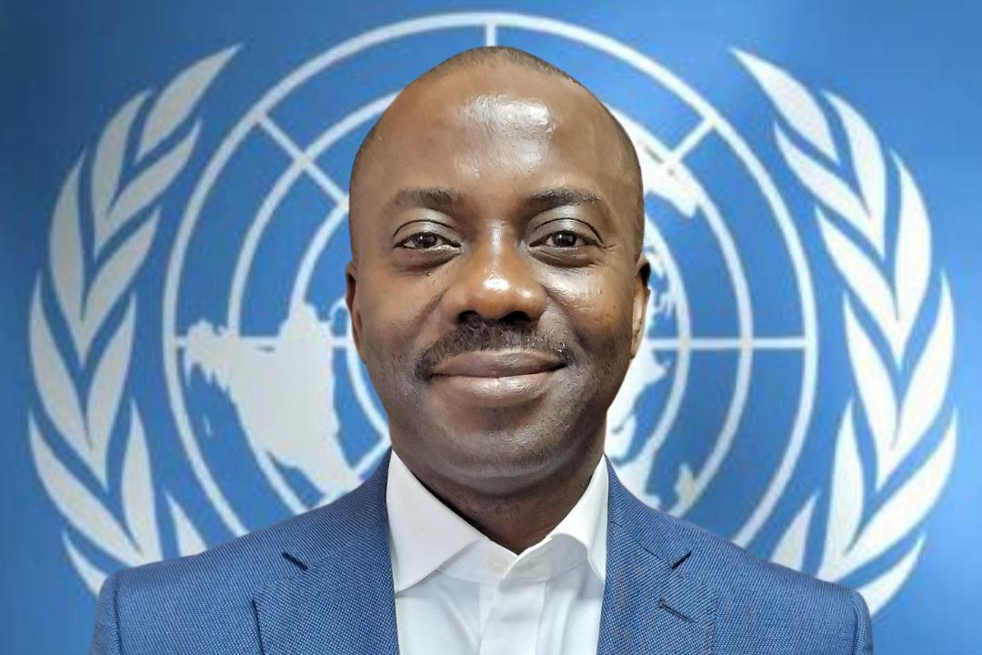 A headshot of a man in a suit stands in front of the UN logo