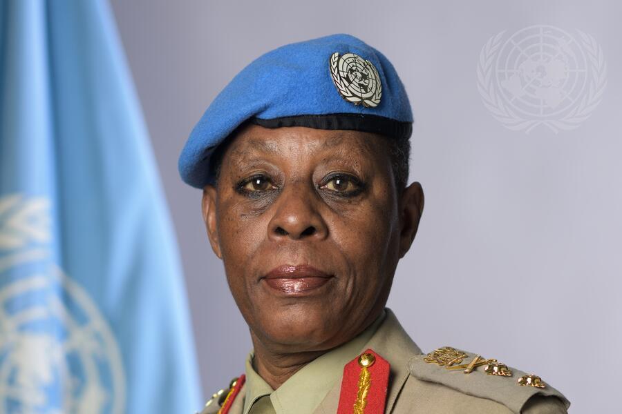 A  woman in military uniform wears a blue beret in front of the UN flag